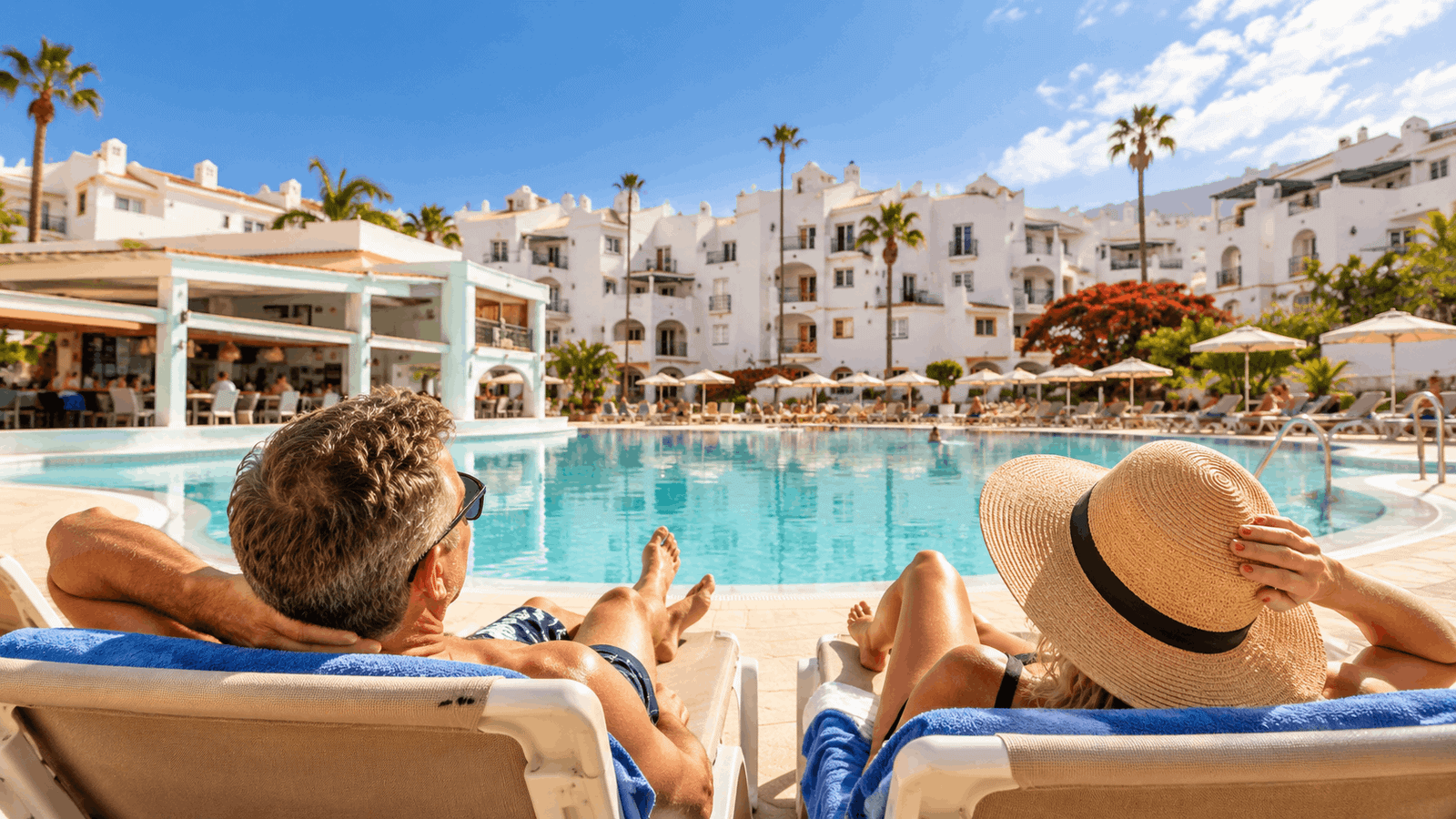 Sunny balcony with a table and chairs overlooking a palm-lined pool and the sea in Tenerife South